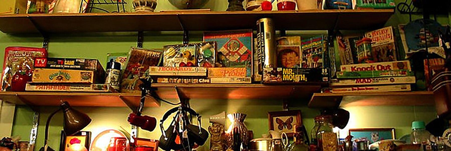 Shelf in an antique shop cluttered with games, lamps, and other household items.
