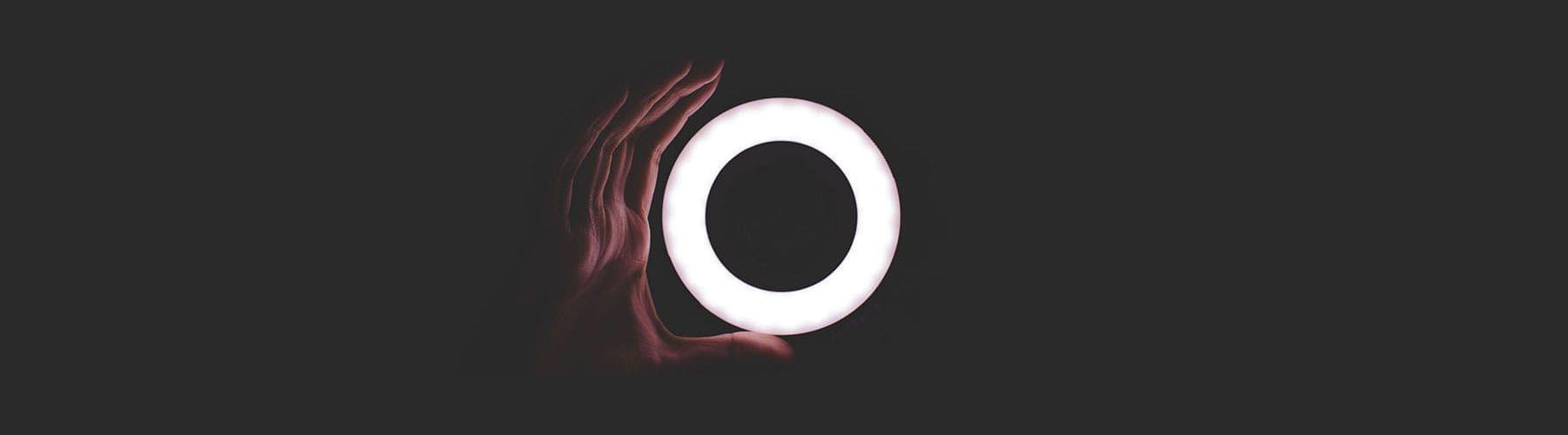 A glowing white circular light held by up by a hand in the darkness.